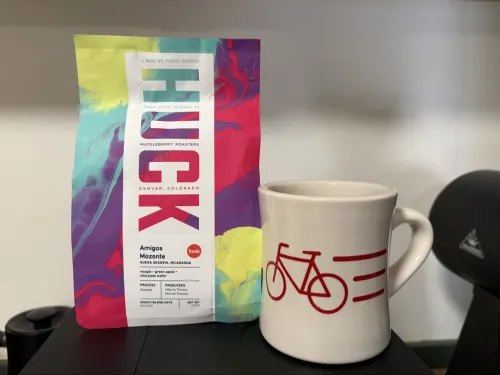 Huckleberry Roasters Amigos coffee bag next to a white mug with a red roadster bicycle.