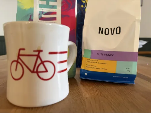 Hand holding a glass cup of coffee with a bag of Novo coffee in the background.