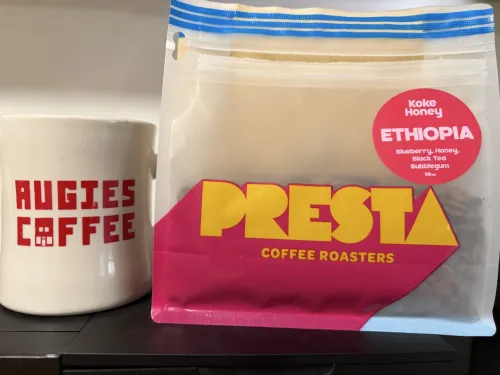 Photo of a Presta coffee bag next to a white Augies Coffee mug
